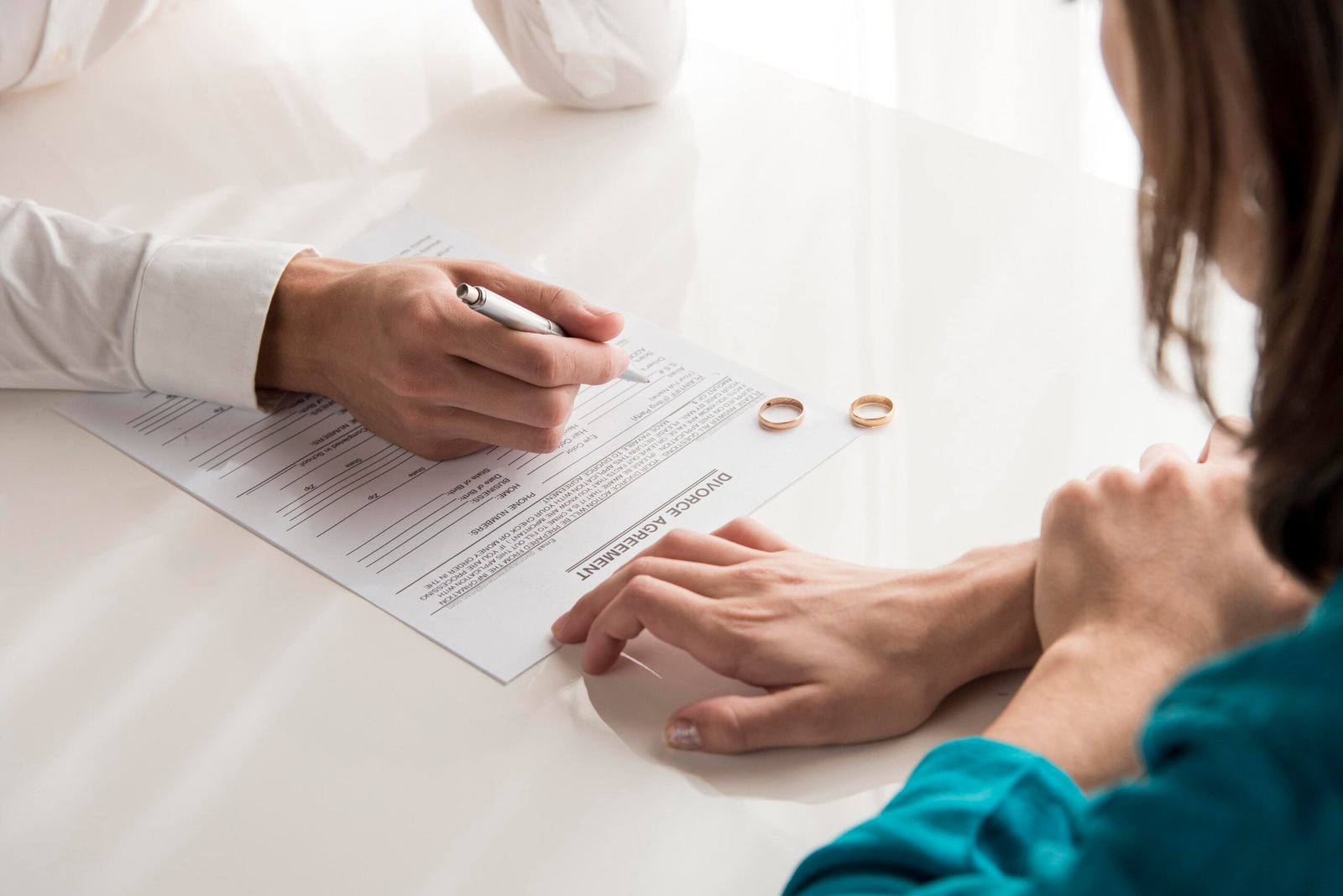 Couple signing divorce papers with rings on table